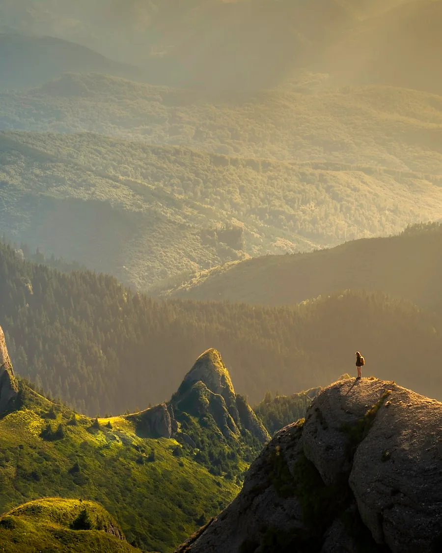 A lone traveller looking out over golden mountains at sunrise